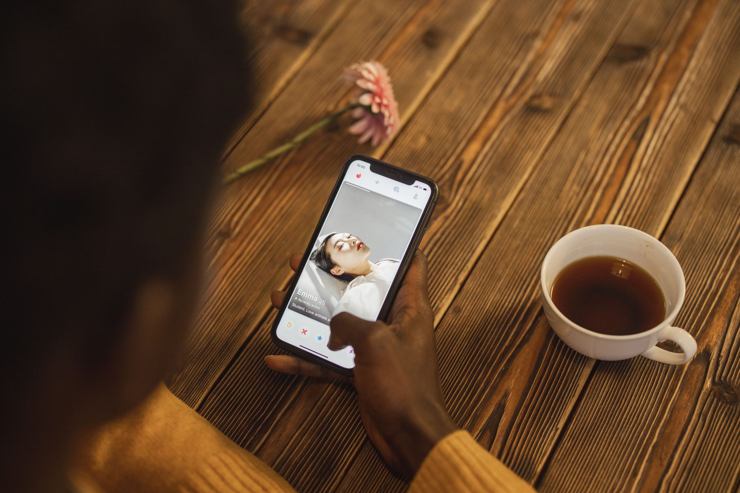 Person using a dating app on a smartphone with a cup of tea nearby, illustrating digitally mediated companionship.