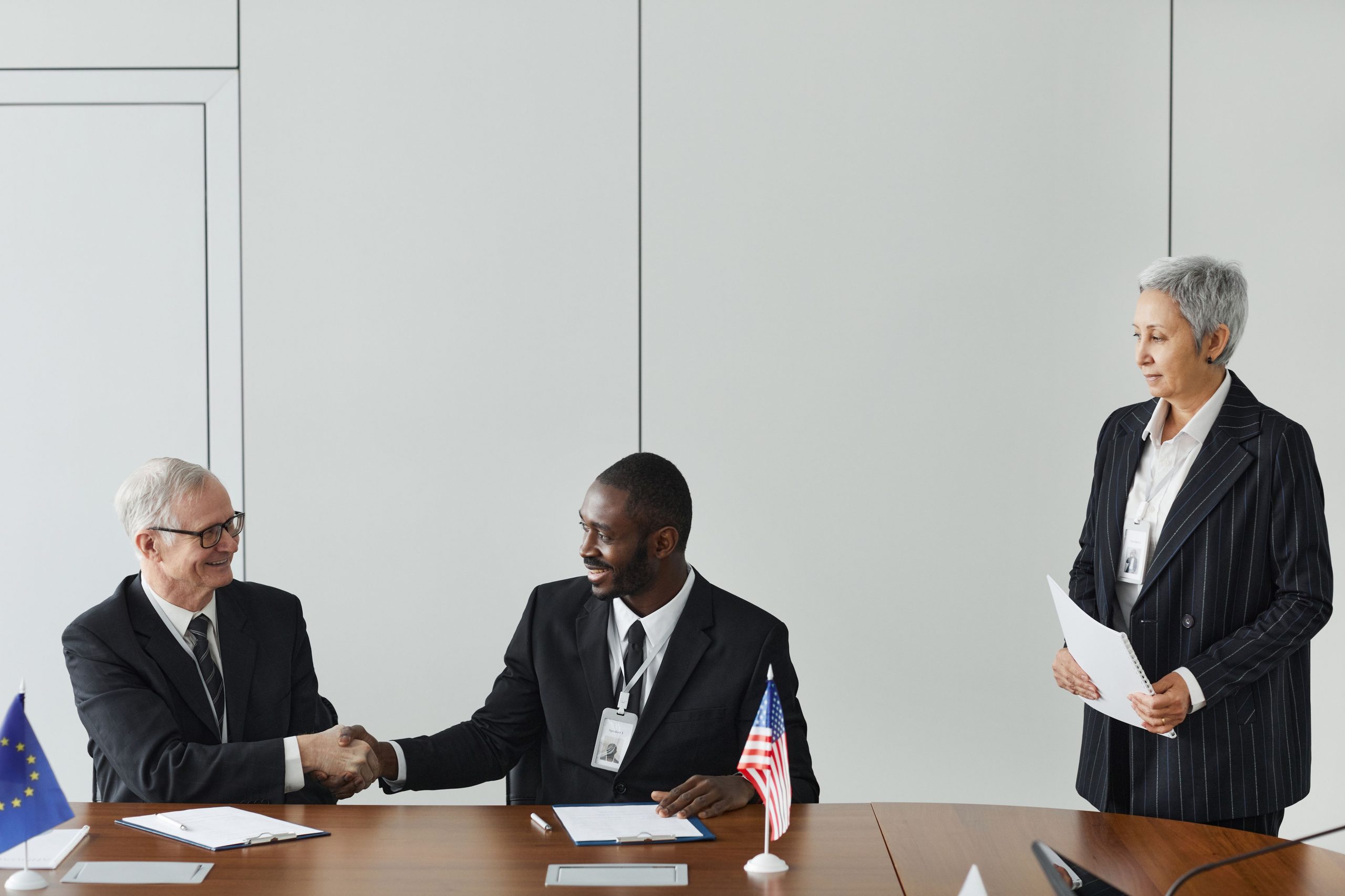 Multinational diplomats signing an international agreement around a table with national flags in the background