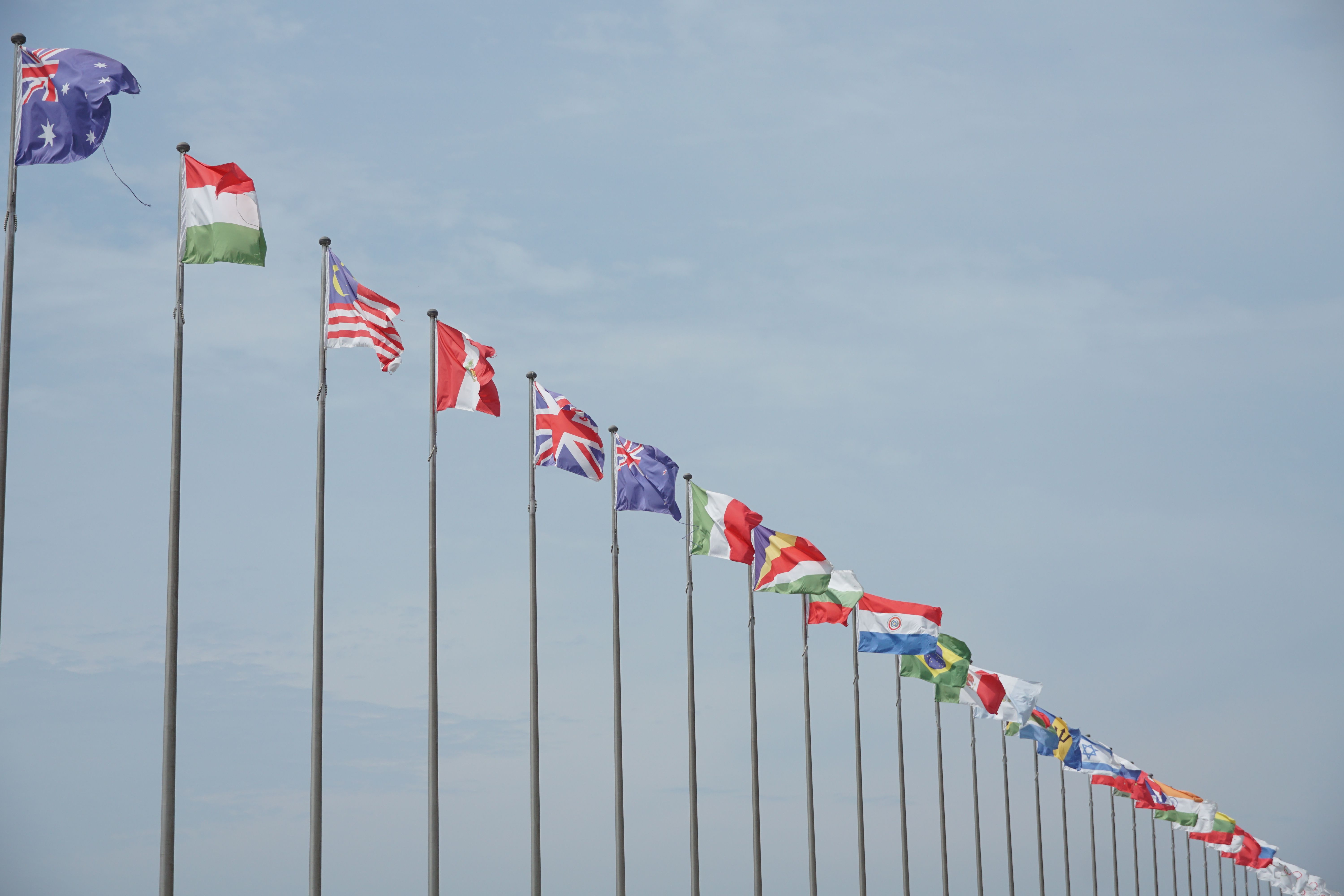 Row of international flags on flagpoles waving against the sky, representing diplomacy between countries
